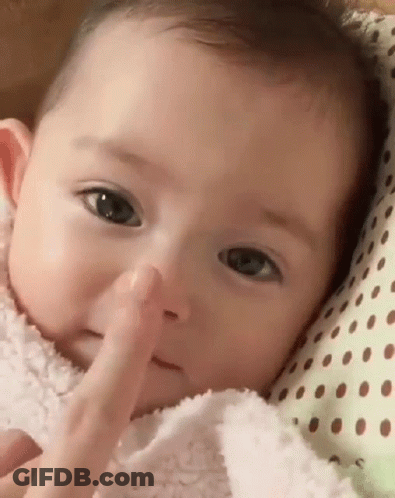 A Baby Is Laying On A Polka Dot Pillow And Touching His Nose . GIF