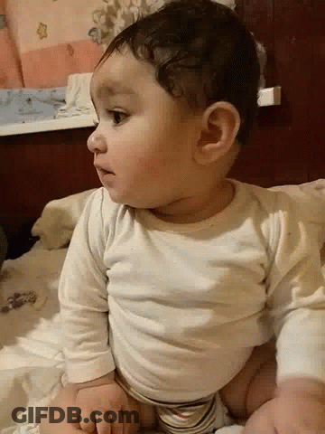 A Baby Is Laying On His Stomach On A Bed GIF
