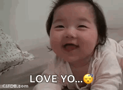 A Baby Is Laying On Its Stomach And Smiling While Saying `` Love You '' . GIF