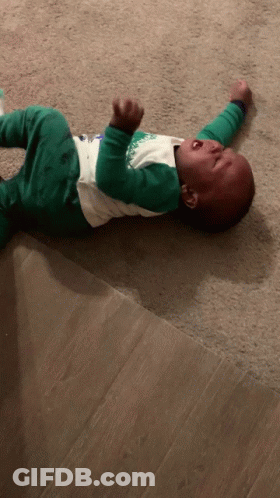 A Baby Is Laying On The Floor Crying And Wearing A Shirt That Says ' Christmas ' On It GIF