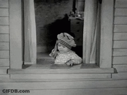 A Baby Is Looking Out Of A Window Wearing A Hat . GIF