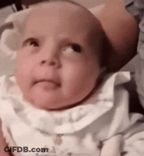 A Baby Is Looking Up At The Camera While Wearing A White Shirt And Bib . GIF