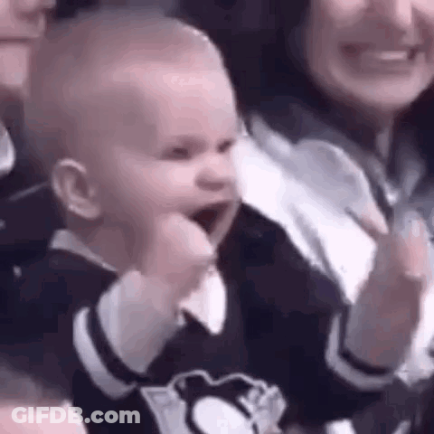 A Baby Is Making A Fist In The Air While Sitting Next To A Woman . GIF