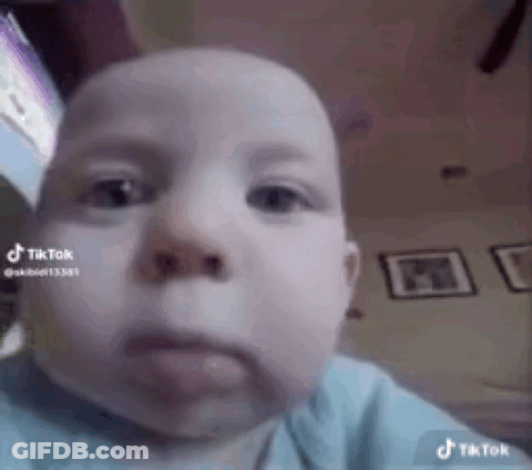 A Baby Is Making A Funny Face While Looking At The Camera In A Living Room . GIF