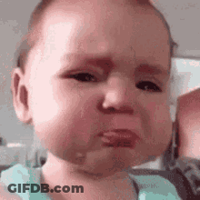 A Baby Is Making A Sad Face While Being Held By A Person . GIF