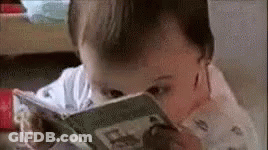 A Baby Is Reading A Book While Sitting On A Table . GIF