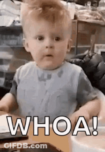 A Baby Is Sitting At A Table And Making A Funny Face While Wearing A Bib And Saying `` Whoa ! '' GIF