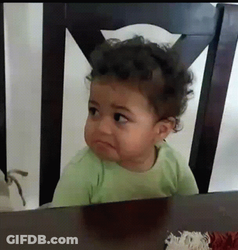 A Baby Is Sitting At A Table With A Sad Look On His Face GIF