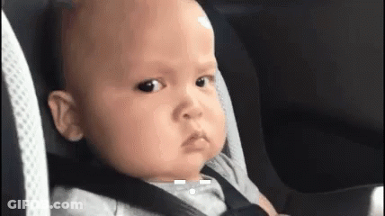 A Baby Is Sitting In A Car Seat With A Seat Belt On Making A Funny Face . GIF