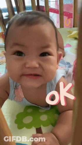 A Baby Is Sitting In A Crib With An Ok Sticker On His Chest GIF