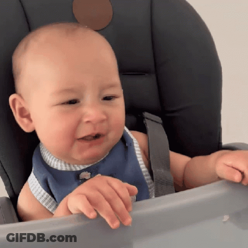 A Baby Is Sitting In A High Chair And Looking At Something GIF