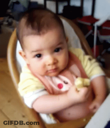 A Baby Is Sitting In A High Chair And Looking At The Camera . GIF