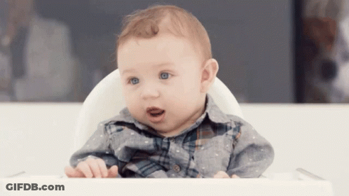 A Baby Is Sitting In A High Chair And Looking At The Camera GIF