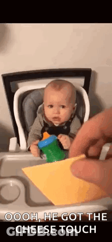 A Baby Is Sitting In A High Chair While A Person Takes A Piece Of Cheese From Him . GIF