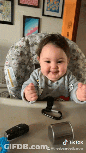 A Baby Is Sitting In A High Chair With A Sticker On His Shirt That Says Anna GIF
