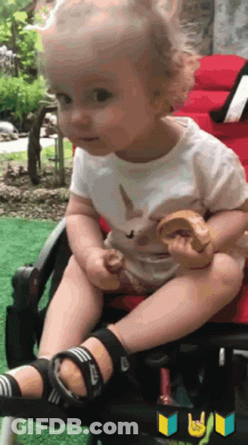 A Baby Is Sitting In A Stroller And Eating A Cookie GIF