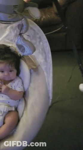 A Baby Is Sitting In A Swing With A White Cover On It GIF