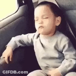 A Baby Is Sitting In The Back Seat Of A Car With His Eyes Closed . GIF