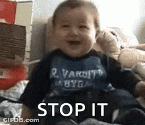 A Baby Is Sitting On A Bed And Smiling While Wearing A Shirt That Says Stop It . GIF