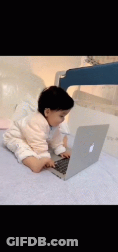 A Baby Is Sitting On A Bed Using An Apple Laptop Computer . GIF