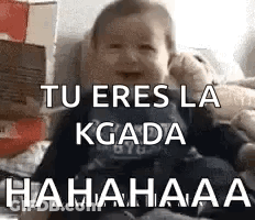 A Baby Is Sitting On A Bed With The Words `` Tu Eres La Kgada Hahahaa '' Written On The Screen . GIF