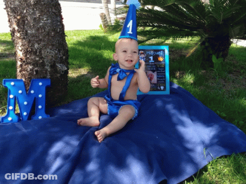 A Baby Is Sitting On A Blue Blanket With A Sign That Says " Miguel " On It GIF