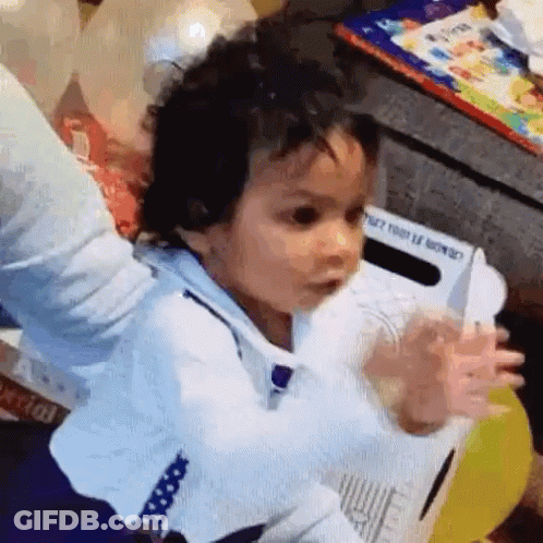 A Baby Is Sitting On A Chair With His Arms Outstretched And A Knife In His Hand . GIF