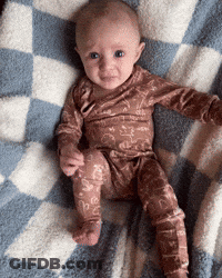 A Baby Is Sitting On A Checkered Blanket GIF
