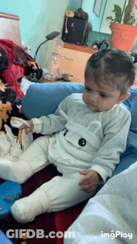 A Baby Is Sitting On A Couch With A Cat On His Shirt GIF