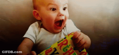 A Baby Is Sitting On A Couch With His Mouth Open And Holding A Birthday Present . GIF