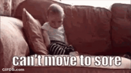 A Baby Is Sitting On A Couch With The Words `` Can 'T Move To Sore '' Written On The Bottom . GIF