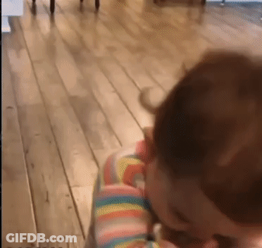 A Baby Is Sitting On A Wooden Floor With A Rainbow Striped Shirt On . GIF