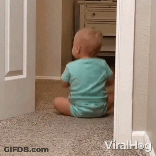 A Baby Is Sitting On The Floor In A Room Looking Out Of A Doorway . GIF