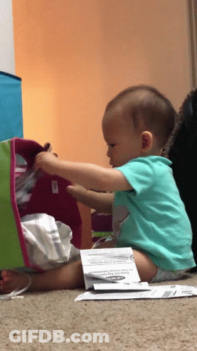 A Baby Is Sitting On The Floor Playing With A Box That Says " For Your Safety " On It GIF