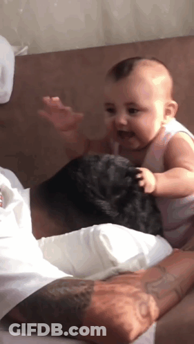 A Baby Is Sitting On The Lap Of A Man GIF
