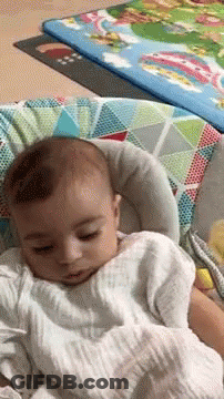 A Baby Is Sleeping In A Bouncer With A Blanket On It . GIF