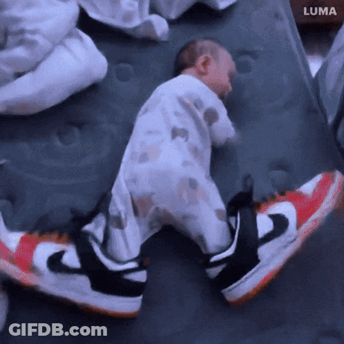 A Baby Is Sleeping On A Mattress Next To A Pair Of Nike Sneakers GIF