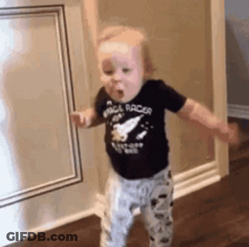 A Baby Is Standing In A Room With His Arms Outstretched And Wearing A Space Racer Shirt . GIF