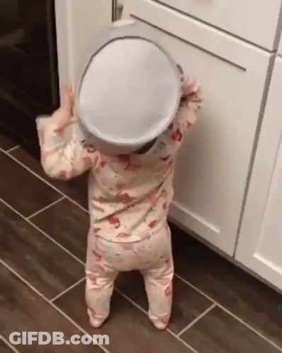 A Baby Is Standing On A Tiled Floor Holding A Pot On Her Head . GIF