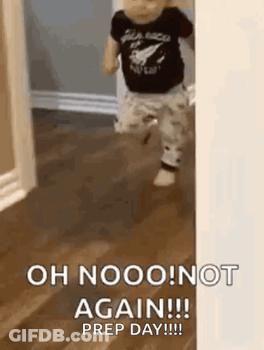 A Baby Is Standing On A Wooden Floor In Front Of A Door . GIF
