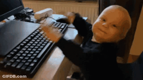 A Baby Is Typing On A Keyboard With A Laptop In The Background GIF