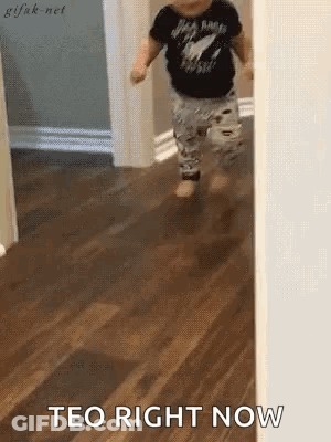 A Baby Is Walking On A Wooden Floor With The Words Teo Right Now Written On The Floor . GIF