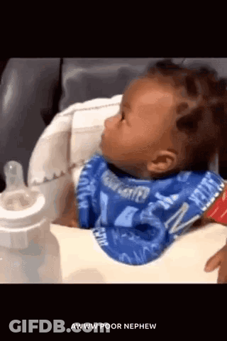 A Baby Is Wearing A Bib And Sitting In A High Chair . GIF