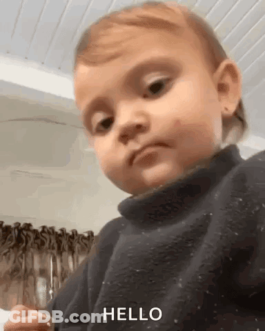 A Baby Is Wearing A Black Sweater And Making A Funny Face . GIF