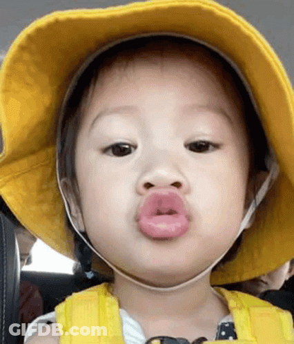 A Baby Is Wearing A Yellow Hat And Making A Funny Face With His Lips . GIF