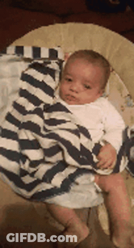 A Baby Is Wrapped In A Striped Blanket And Sitting In A Bouncer . GIF