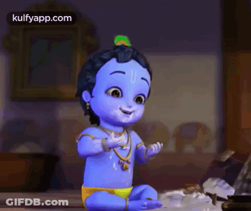 A Baby Krishna With A Peacock Feather On His Head Is Sitting On A Bed Talking On A Cell Phone . GIF
