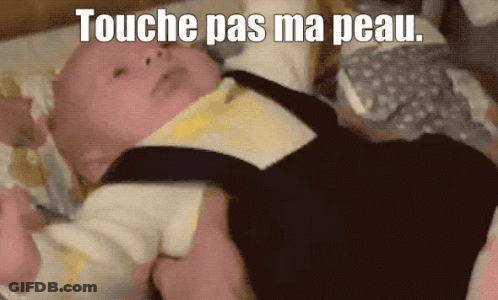 A Baby Laying On A Bed With The Words " Touche Pas Ma Peau " Written Above It GIF