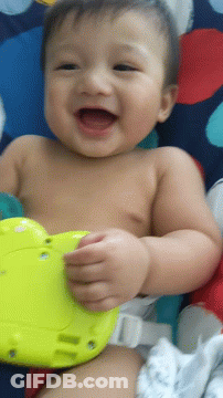 A Baby Laying On A Blanket With A Yellow Toy GIF
