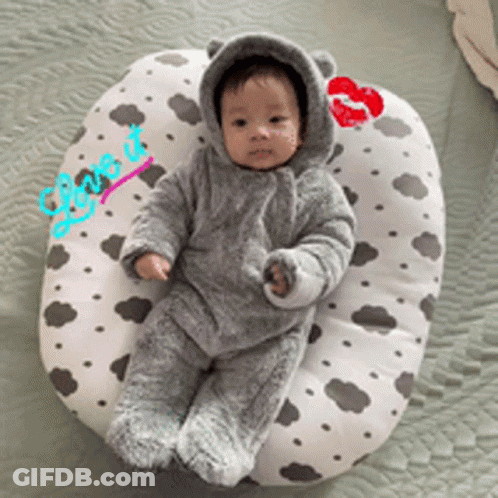 A Baby Wearing A Bear Costume Is Laying On A Pillow With A Kiss On It GIF